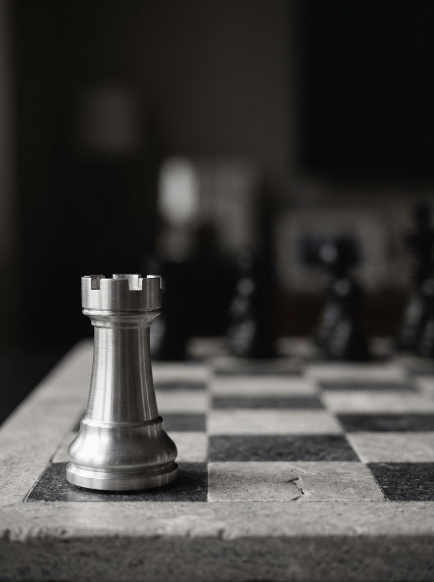 A brushed-aluminium chess rook on the back rank of a grey stone chessboard.
